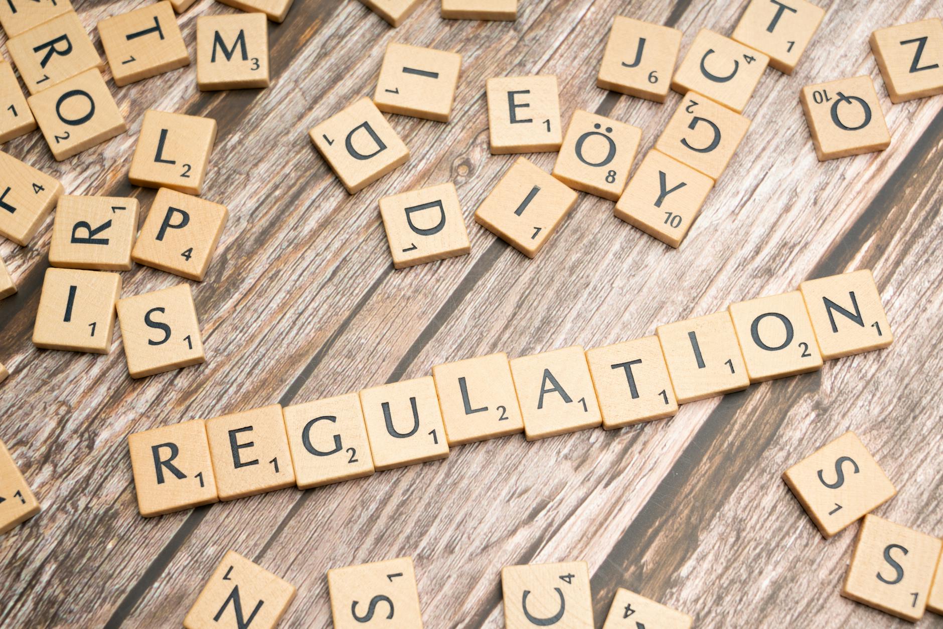 A collection of wooden letter tiles scattered on a wooden surface, with the word 'REGULATION' prominently displayed in the center.